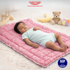 Baby sleeping on a pink mat with a teddy bear and toy in the background, featuring the TINY TYKE brand.
